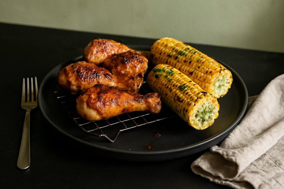Maiskolven van de BBQ met kruidenboter en kip drumsticks